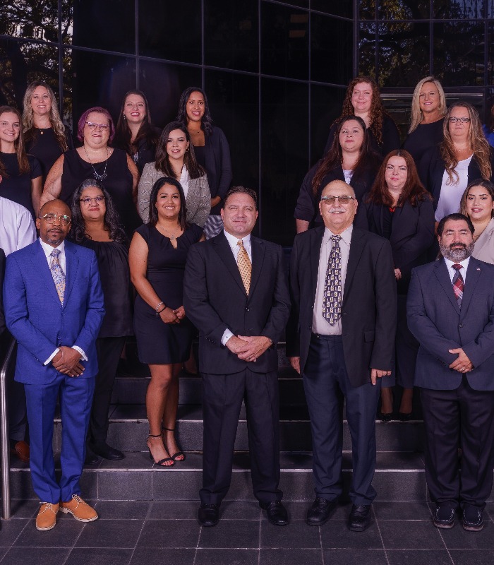 Meet Our Team - Professional and Welcoming Group at a Conference Table Faces the Camera, Team Leader Sitting on the Table with Arms Folded